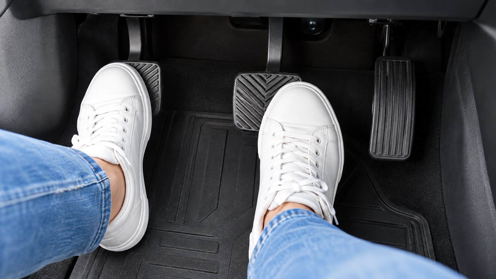 A driver's feet wearing white sneakers while operating the car pedals to practice safe driving techniques.