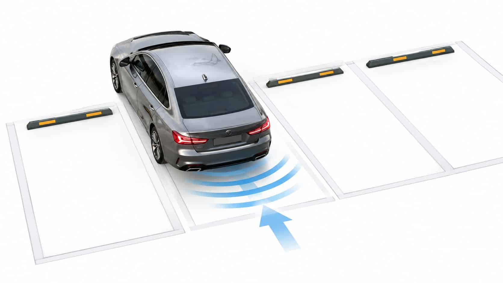 A silver sedan performing a reverse parking maneuver into a marked parking space with sensor detection visualization.
