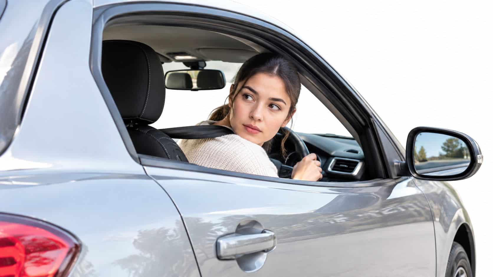 A young female driver looking back over her shoulder while reversing a car for parking.