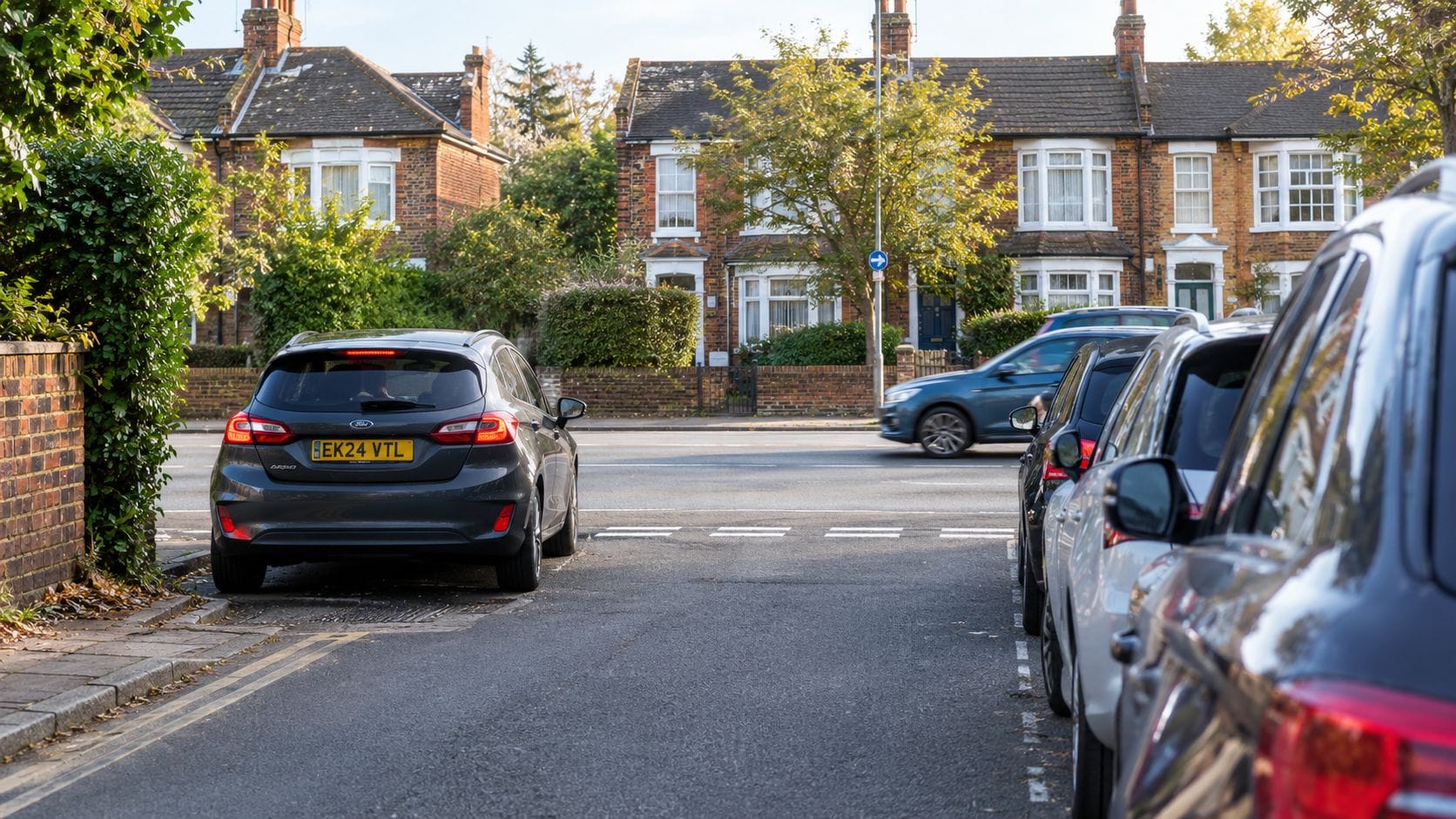 A gray Ford car parked on a suburban residential street next to other parked vehicles near a road.